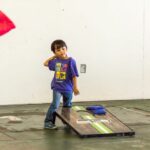 A young boy winds up to throw a bean bag, while another bean bag can be seen in the air beside him.