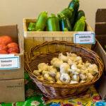 A basket of garlic next to boxes of zucchini and tomatoes.