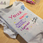 A gray sweater shirt painted with polka dots and phrases like "Your worth it," "I survived," and "I am strong!"