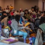 A crowd of people sit in chairs watching a presentation in a conference room.