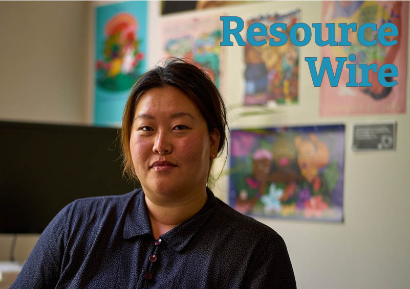 A woman in a blue collared shirt sits in front of a blank computer monitor and a wall covered in posters. The words "Resource Wire" appear above her.