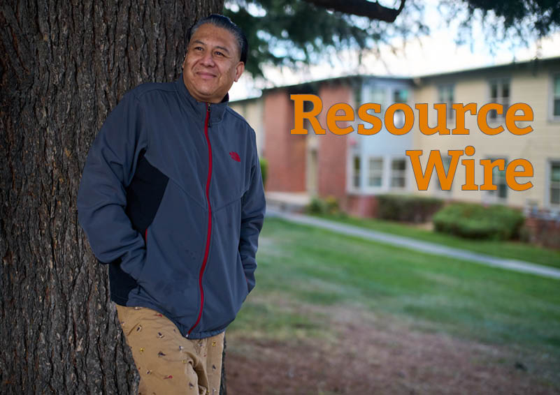 A man in a blue sweater leans against a thick tree trunk with an apartment building in the background. Beside him are the words "Resource Wire"