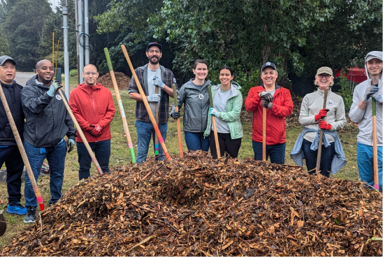 Volunteers posing with shovels behind a pile of mulch